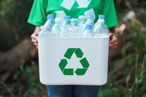 woman collecting garbage and holding a recycle bin with plastic bottles in the outdoors
