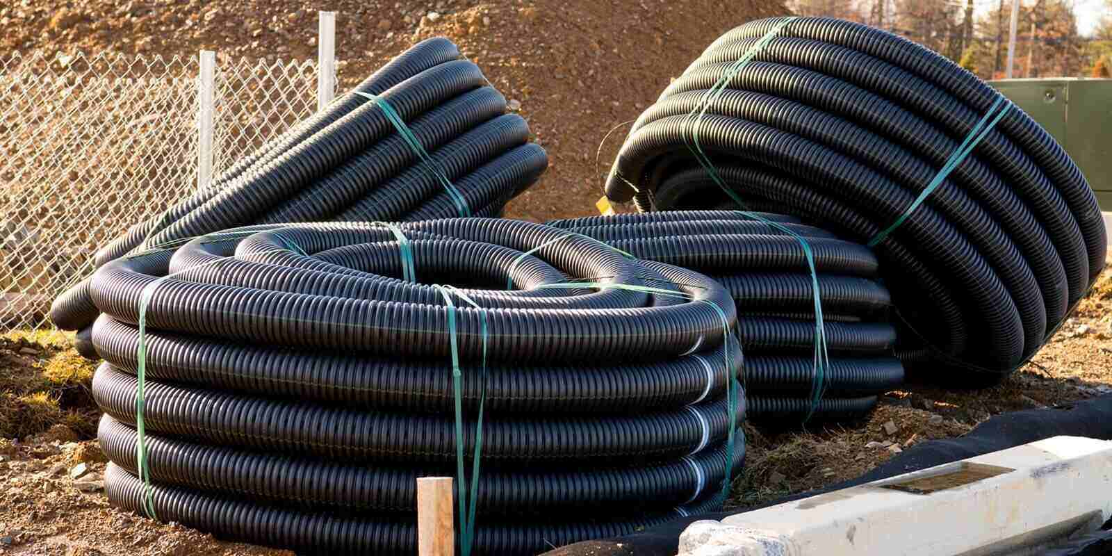many rolled coils of new black corrugated plastic electric plumbing drainage pipe prepared for installation near building construction site